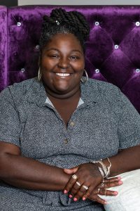 Sakara Wages smiling in a grey shirt with a purple background