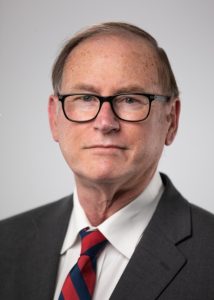 Michael Daley in dark grey suit, red tie, and black glasses