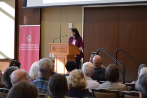 Dr. Anna Gassman-Pines standing at podium speaking into microphone