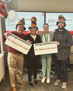 Four people, three wearing Dr. Suess hats, holding two signs that read: Congratulations, Dr. Kiley is in the house!