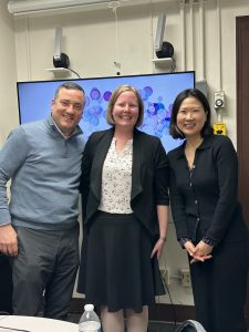 Three people standing in front of a video screen. 