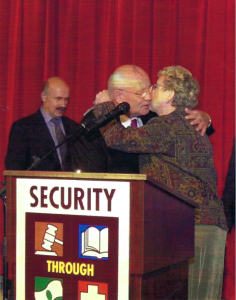 Soviet Leader, Mikhail Gorbachev, thanking alum Sandy McCormick for her work with World Services, La Crosse – photo taken in La Crosse. They are behind a podium, hugging, in front of a red curtain.