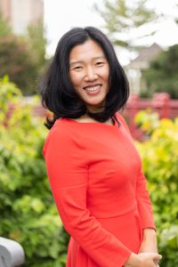 Photo of Seungmi L. Cho wearing red dress in front of green bushes.