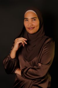 Headshot of Melissa Mueller-Douglas, MSW ’11 in front of a black screen wearing a brown shirt and hijab.