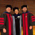 Dr. Pac standing with two PhD advisees at graduation wearing academic robes.