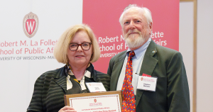 Molly Collins Offner (left) and Stephen Webster holding the Alumni of Distinction award in front of a school banner.